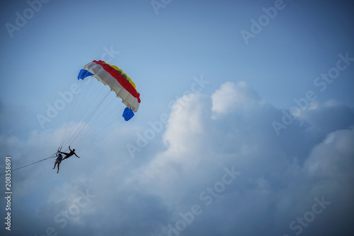Two tourists are playing the parasailing in the sky during summer.