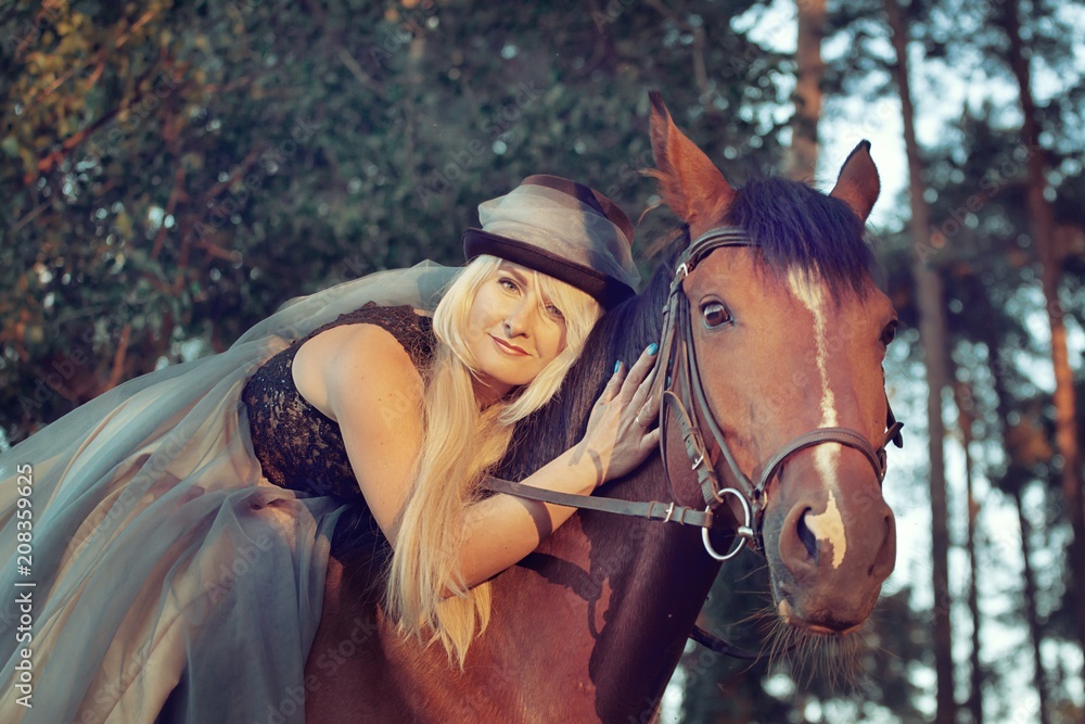 Obraz premium beautiful girl blond rider in hat in dress on horse walk in coniferous forest