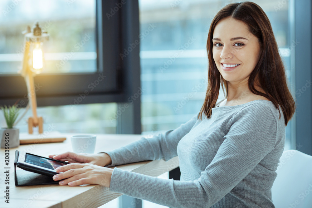 High spirited. Amazing female person keeping smile on her face and turning head while using her tablet High spirited. Amazing female person keeping smile on her face and turning head while using her tablet