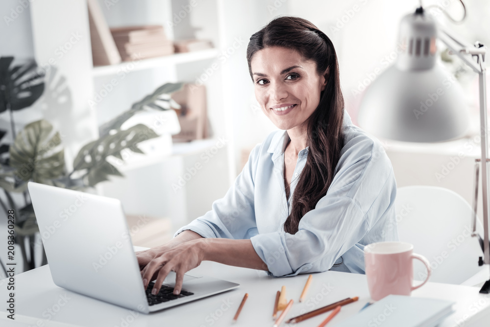 Joyful mood. Pretty longhaired brunette demonstrating her emotions while sitting at her workplace Joyful mood. Pretty longhaired brunette demonstrating her emotions while sitting at her workplace