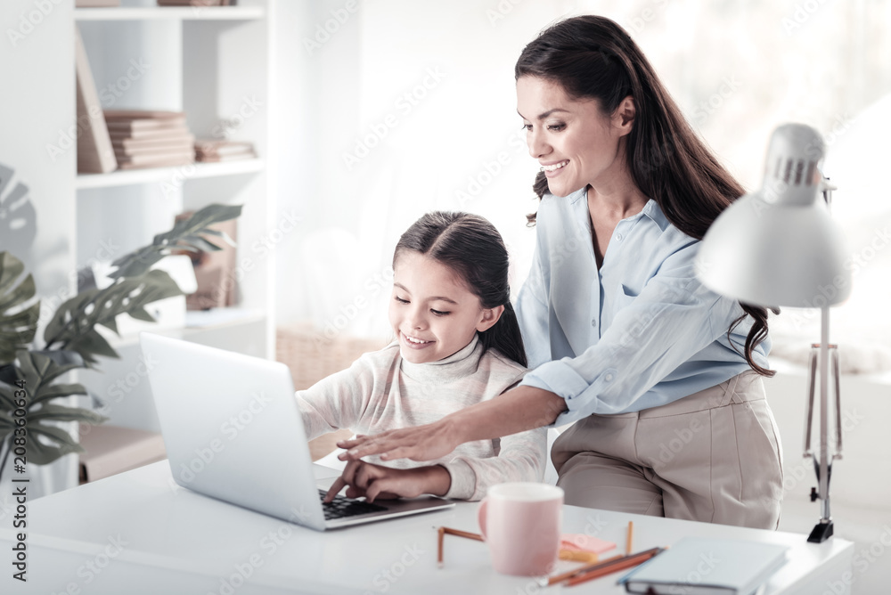 Look here. Cheerful young woman keeping smile on her face while helping her pupil Look here. Cheerful young woman keeping smile on her face while helping her pupil