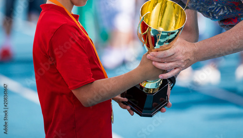 Child in a sportswear receiving a golden cup. Young athlete winning the sports school competition. Boy with golden medal getting an award for the best player of the tournament photo