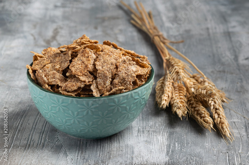 Wheat flakes in a ceramic bowl with ears of wheat on gray background. Horizontal. Copy space photo