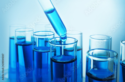 Dripping blue liquid into test tubes on color background
