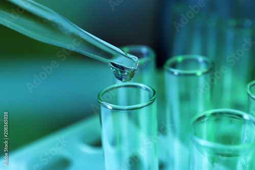 Pipette dripping sample into test tube on color background, closeup