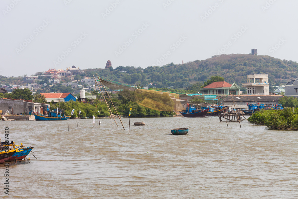 View of landscape of hills with Po Sah Inu Cham Towers, Buddhist temple, town houses and river with fishing net and boats near Mui Ne, Binh Thuan province in South Vietnam.