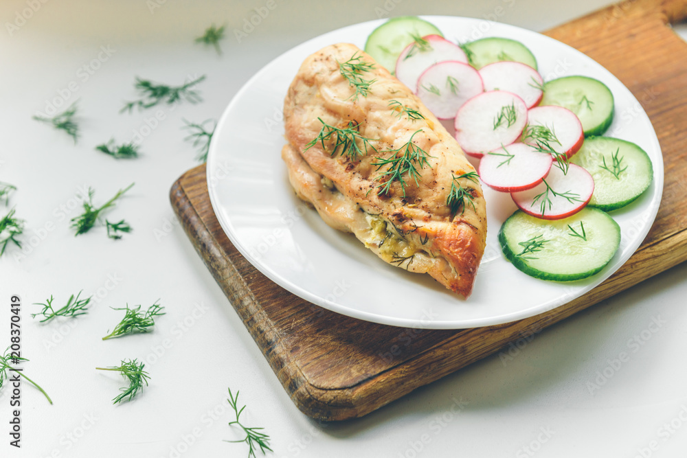 Baked chicken breast with cheese, cucumber and red radish on white plate. Healthy diet protein food. Baked chicken breast with cheese, cucumber and red radish on white plate. Healthy diet protein food.