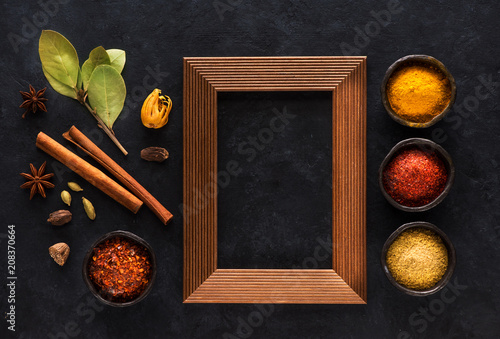 Fototapeta Naklejka Na Ścianę i Meble -  Indian spices and empty wooden frame for text on black concrete background, top view, flat lay