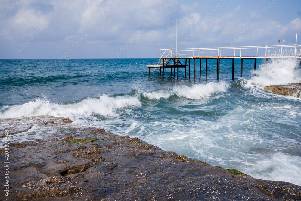 Waves running to the shore with white foam and pier at the background