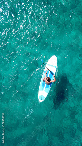 Aerial drone bird's eye view of a man exercising sup board in turquoise tropical clear waters