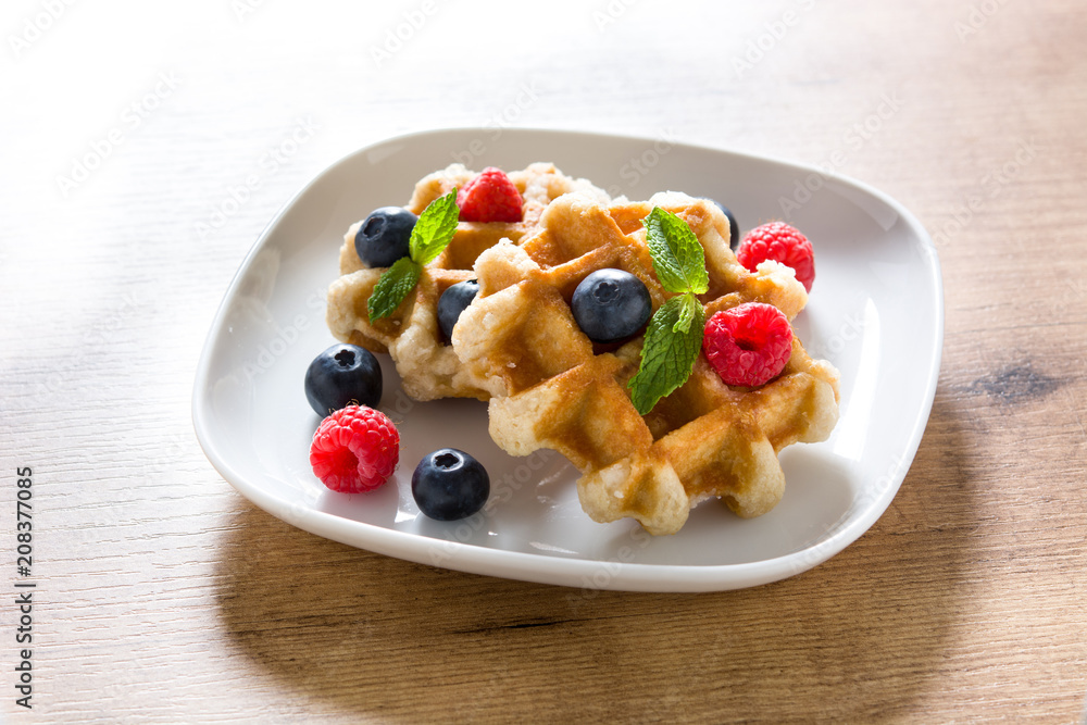 Traditional belgian waffles with blueberries and raspberries on wooden table Traditional belgian waffles with blueberries and raspberries on wooden table