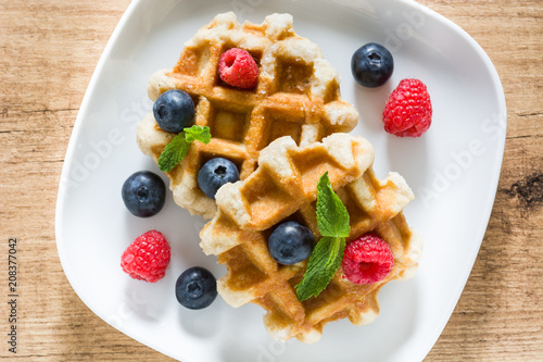 Traditional belgian waffles with blueberries and raspberries on wooden table. Top view
