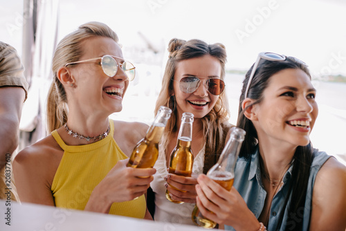 smiling young women drinking beer at beach bar