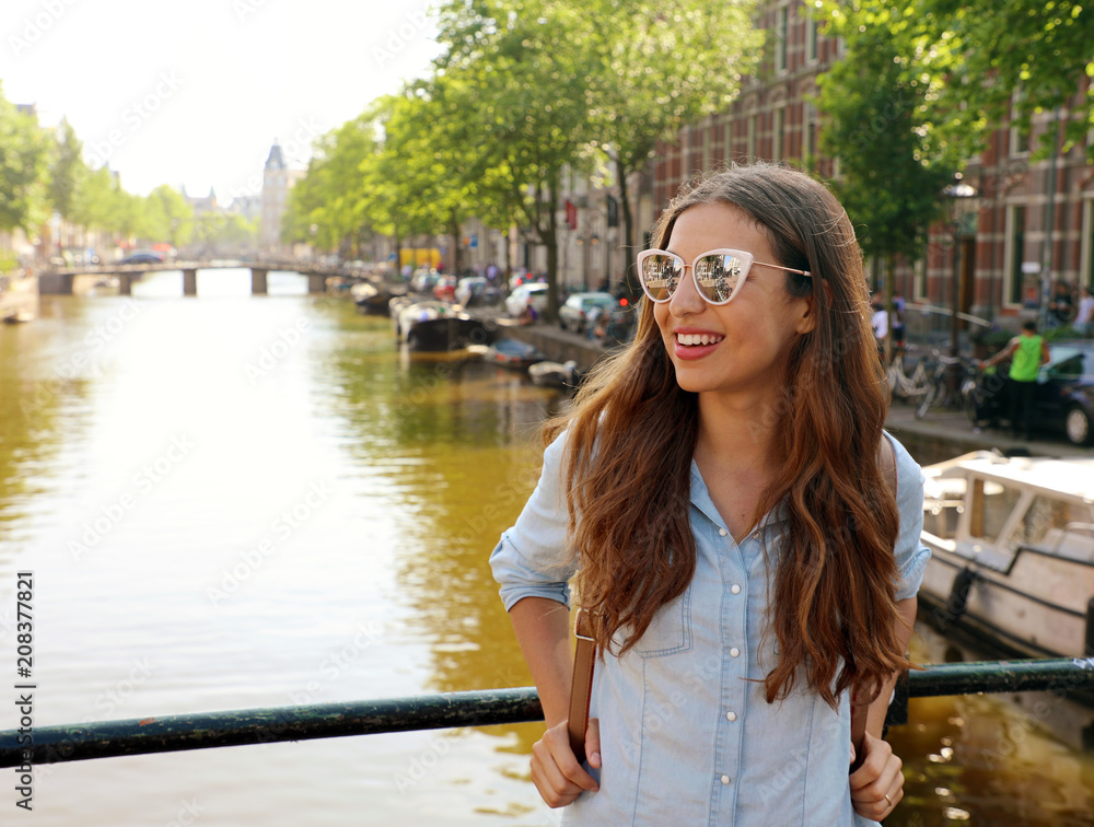 Portrait of beautiful cheerful girl with sunglasses looking to the side on one of typical Amsterdam channels, Netherlands, Europe