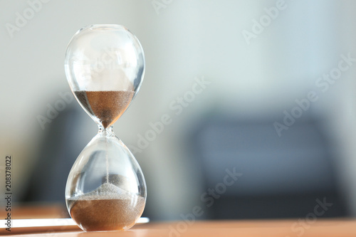 Hourglass on table against blurred background. Time management concept