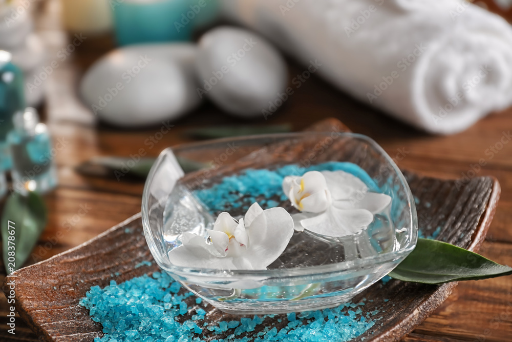 Glass bowl of water with flowers and sea salt for spa treatment on tray Glass bowl of water with flowers and sea salt for spa treatment on tray
