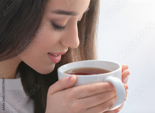 Beautiful young woman with cup of hot tea at home, closeup