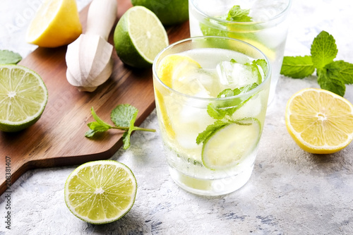 Two glasses of refreshing non alcoholic mojito lemonade drink with organic lemon, lime slices, mint leaves, straw, ice cubes on grunged grey concrete table background. Close up, top view, copy space. © Evrymmnt
