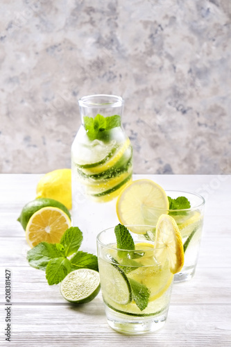 Vintage bottle with two glasses of refreshing non alcoholic mojito lemonade drink with lemon, lime slices, mint leaves, straw, ice on wooden table, concrete background. Close up, top view, copy space.