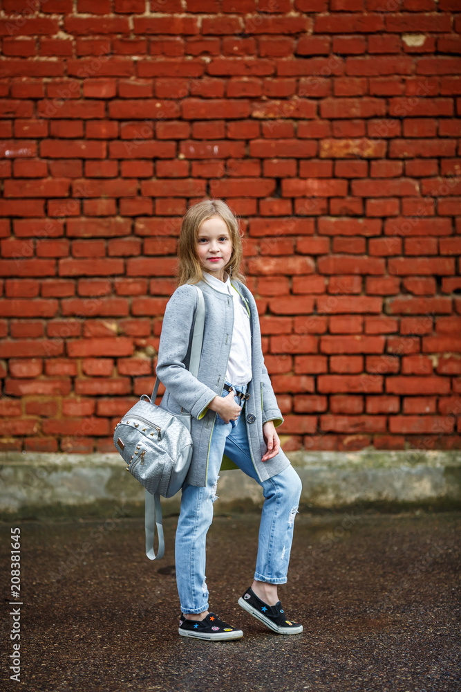 portrait of little beautiful stylish kid girl with backpack near red brick wall as background