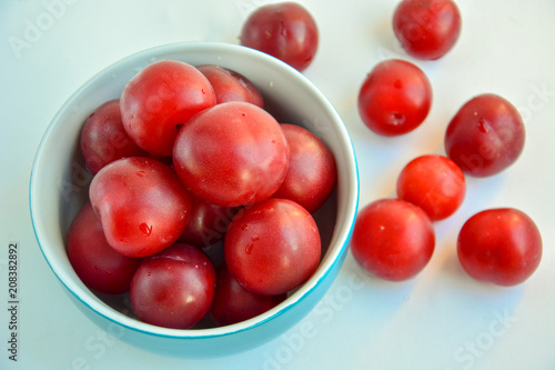 Ripe red plums in a blue ceramic cup on a light background. View from above