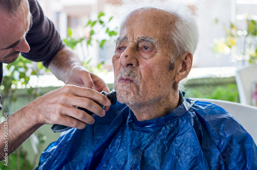 Old man getting his beard shaved by young skilled man at home