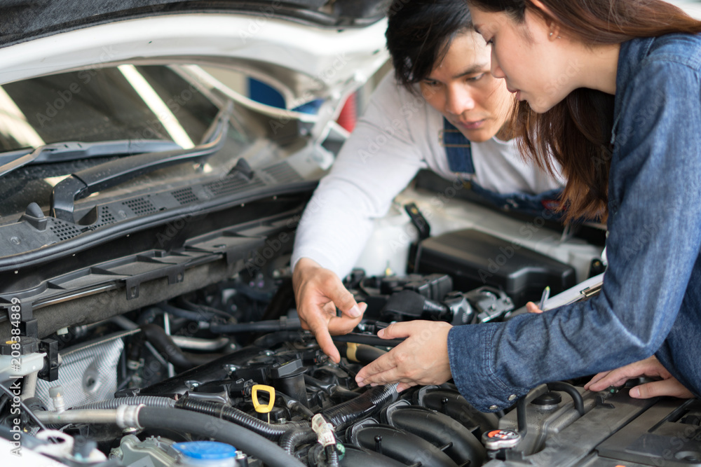 A man mechanic and woman customer look at the car hood and discuss repairs. A man mechanic and woman customer look at the car hood and discuss repairs.