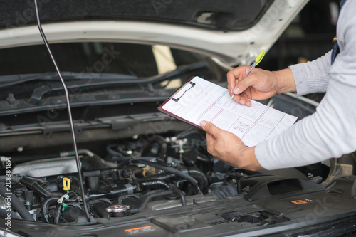 Mechanic engineer hand holding checklist paper and taking a note on clipboard with car engine background.