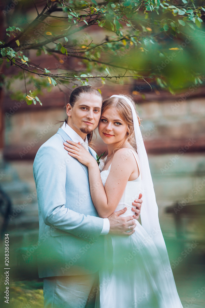 Romantic couple on valentine's day. Man hug a woman in back against the backdrop of a wooden wall of the house. Love story concept. Wedding day of newlyweds bride and groom. Romantic couple on valentine's day. Man hug a woman in back against the backdrop of a wooden wall of the house. Love story concept. Wedding day of newlyweds bride and groom.