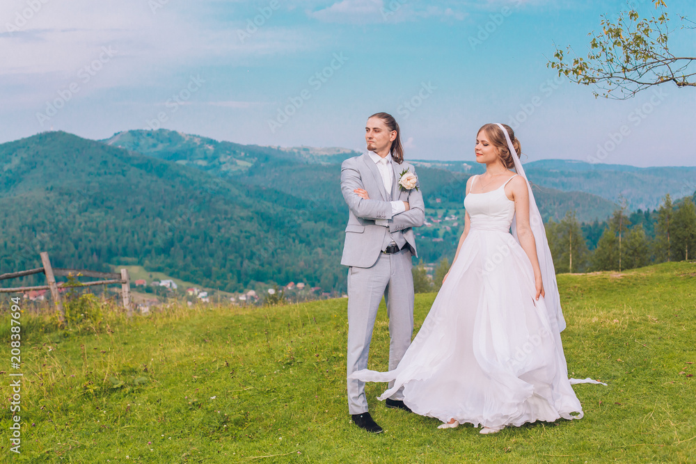 Handsome groom is gently holding his elegant new wife under pine tree. Mountain landscape. Young couple. Wedding day. 