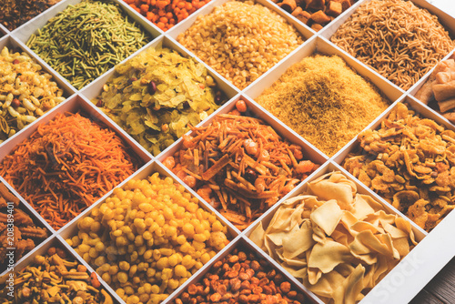 Indian Tea-time snacks like sev, chivda, farsan, mixture, boondi, bakarwadi etc served in white wooden box with cells. selective focus photo