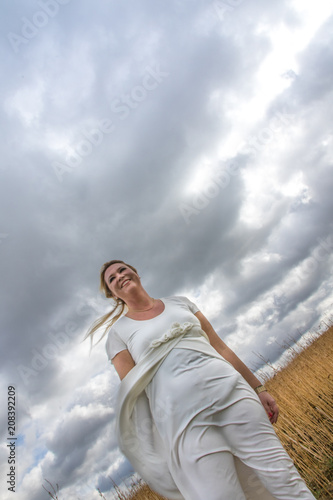 Lebensfreude - Frau in weißem Kleid vor bewölktem Himmel lächelt