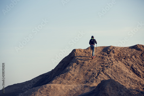 Full-length photo from back of woman growing tourist with backpack and walking sticks on mountain