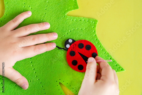 Child making felt soft toy of green leaf and red ladybag . Child DIY activity. Close-up. Children handicraft concept photo