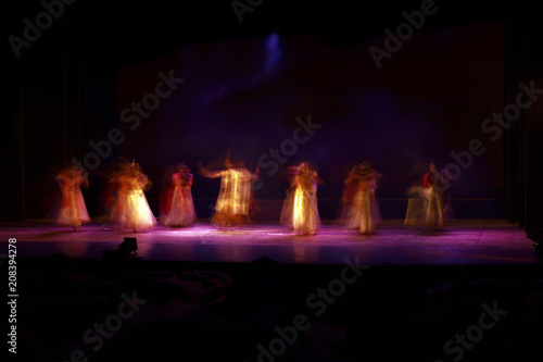 A group of people dancing on stage against black background. 