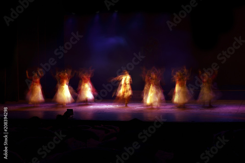 A group of people dancing on stage against black background. 