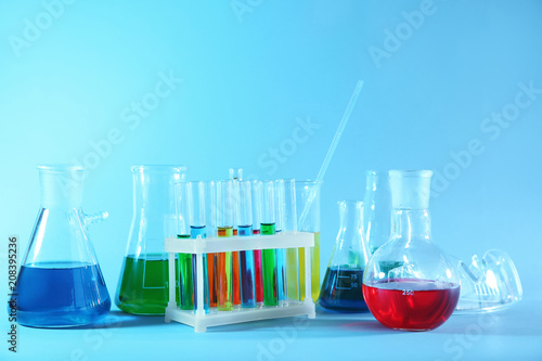 Chemical glassware with colorful samples on color background