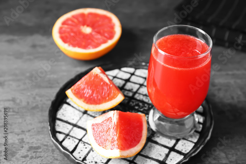 Fresh juice in glass and sliced citrus fruit on grey background