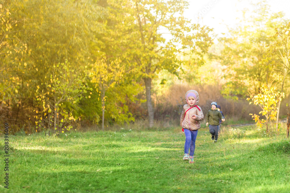 Little blond caucasian girl running in park or forest on bright autumn day. Child having fun playing outdoors. Happy healthy childhood activity and leisure concept Little blond caucasian girl running in park or forest on bright autumn day. Child having fun playing outdoors. Happy healthy childhood activity and leisure concept