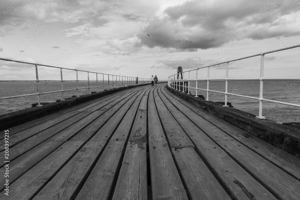 Black and white image of two women walking along a seafront pier