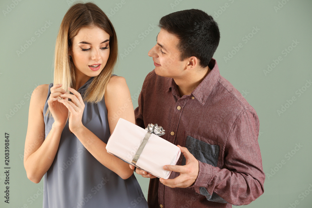 Young man giving present to his beloved girlfriend on color background Young man giving present to his beloved girlfriend on color background