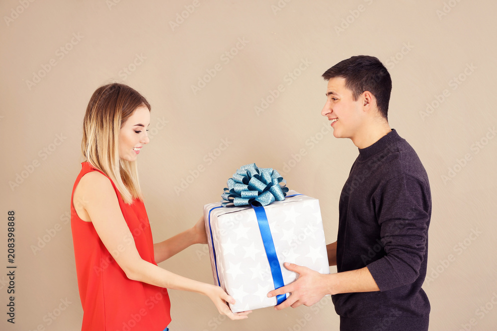 Young man giving present to his beloved girlfriend on color background Young man giving present to his beloved girlfriend on color background