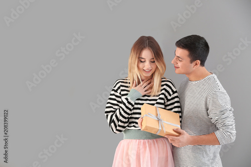 Young man giving present to his beloved girlfriend on grey background