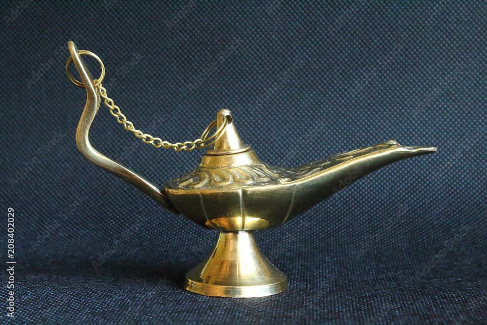 A metallic golden magic lamp of aladdin. Close-up. Isolated object on a black background. A metallic golden magic lamp of aladdin. Close-up. Isolated object on a black background.