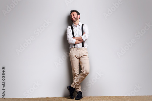 Full length happy man with suspenders laughing against gray background