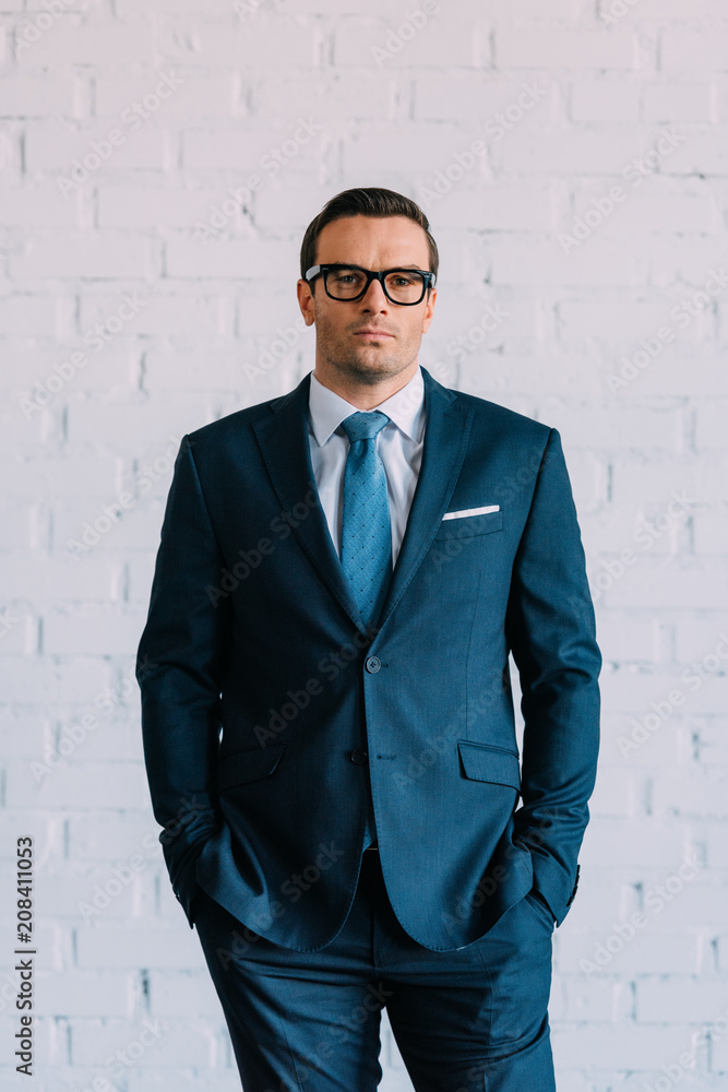 confident middle aged businessman in suit and eyeglasses standing with hands in pockets and looking at camera confident middle aged businessman in suit and eyeglasses standing with hands in pockets and looking at camera