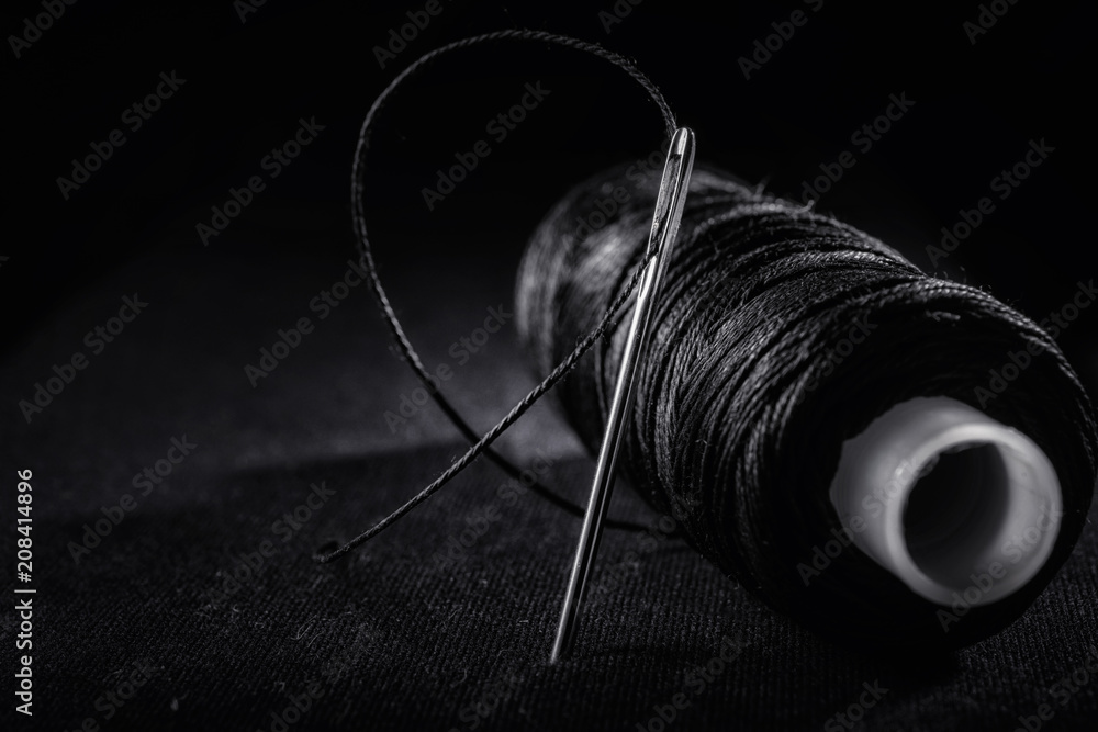 Needle and bobbin with black thread on black background Stock Photo