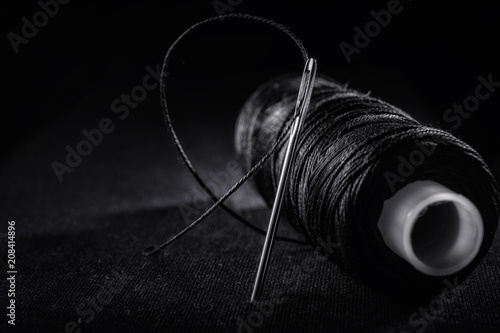 Needle and bobbin with black thread on black background