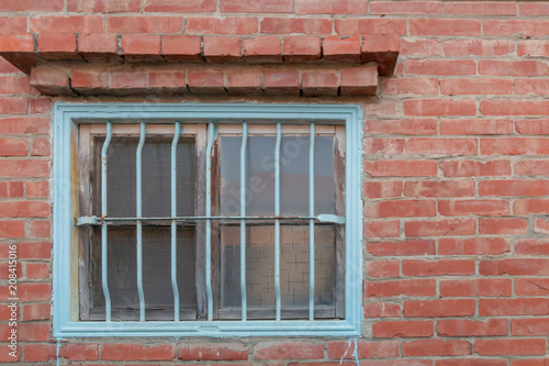 Traditional Asian metal window security covering for a horizontal window. It is painted blue. The window is placed in a brick building. There is a brick overhang above the window.