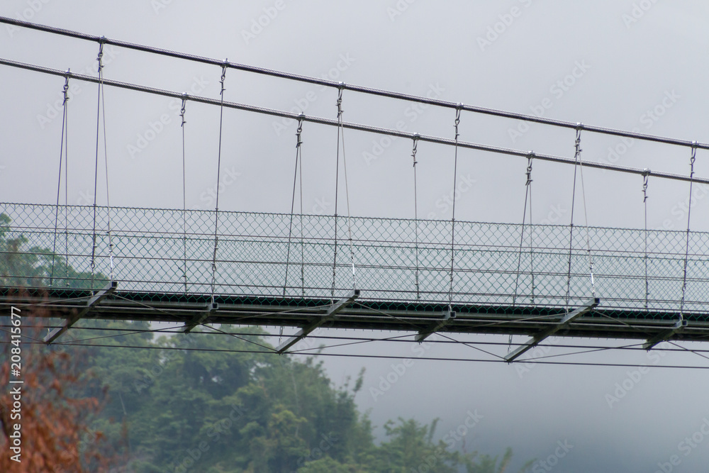 Metal and wire suspension bridge. The background is foggy and trees. Metal and wire suspension bridge. The background is foggy and trees.